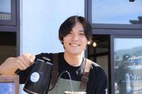 黒色のシャツにエプロンを着用し、笑顔で珈琲を作っている松橋 樹さんの上半身の写真