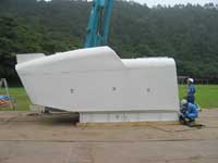 水色のクレーンの手前にヘルメットを被った作業員の背丈より大きなナセルが地面に置かれている写真