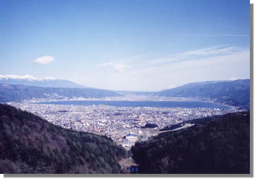 中央に大きな池があり四方を山に囲まれている岡谷市全体の写真