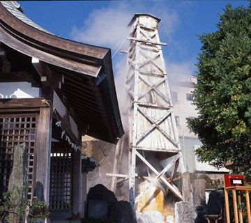 白色の外観の櫓の上からモクモクとした煙が立ち上がっている温泉場の写真