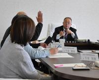 奥に委員長が座る会議室内で、左側にいる参加者が挙手しながら意見交換を行う様子の写真
