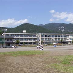 グラウンドで体育の授業を受けている生徒たち、校舎の後ろには山々が連なる東伊豆町立熱川中学校の外観写真