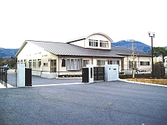 窓の多い平屋で、三角屋根の一部が出っ張って半円形の窓付きの2階部分があるひがしいず幼稚園の外観写真