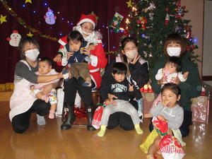 クリスマスツリーの前で、子供たちとサンタに扮した女性の方や保護者の方が集まっている写真
