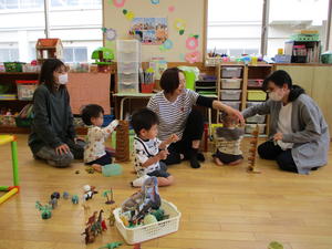 恐竜のフィギュアで遊ぶ3人の子供たちと、それを見守る3人のお母さんの写真