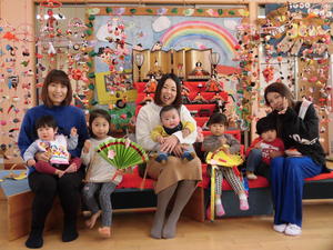 ひな人形が飾られたひな壇の前に座る5人の子供たちと保護者の方の写真