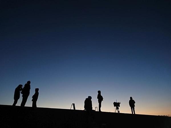 うす暗い中、6名の人々が遠くを見つめている様子を手前から写した写真