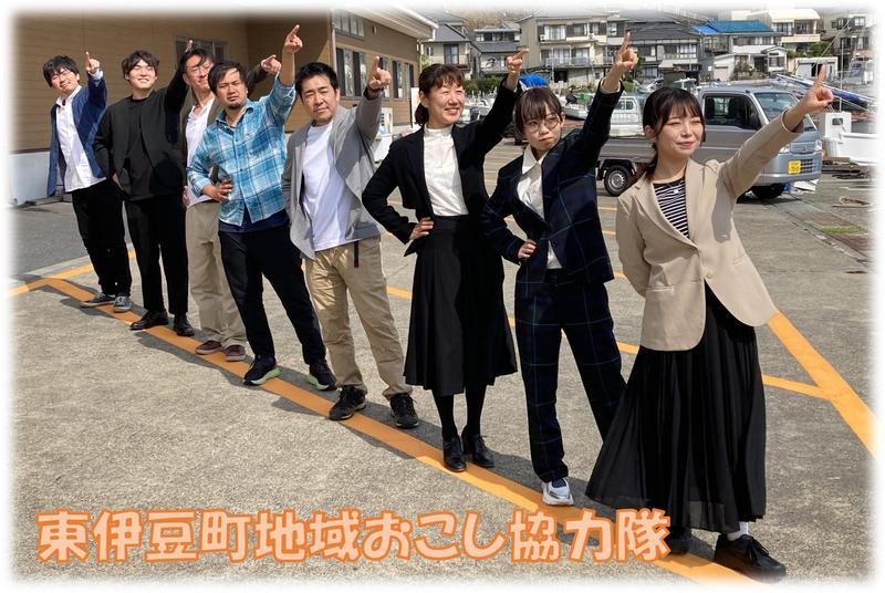 駐車場のオレンジ色のラインに沿って東伊豆町の8名の地域おこし協力隊員が並び、右斜めに向かって左手の人差し指を指している写真