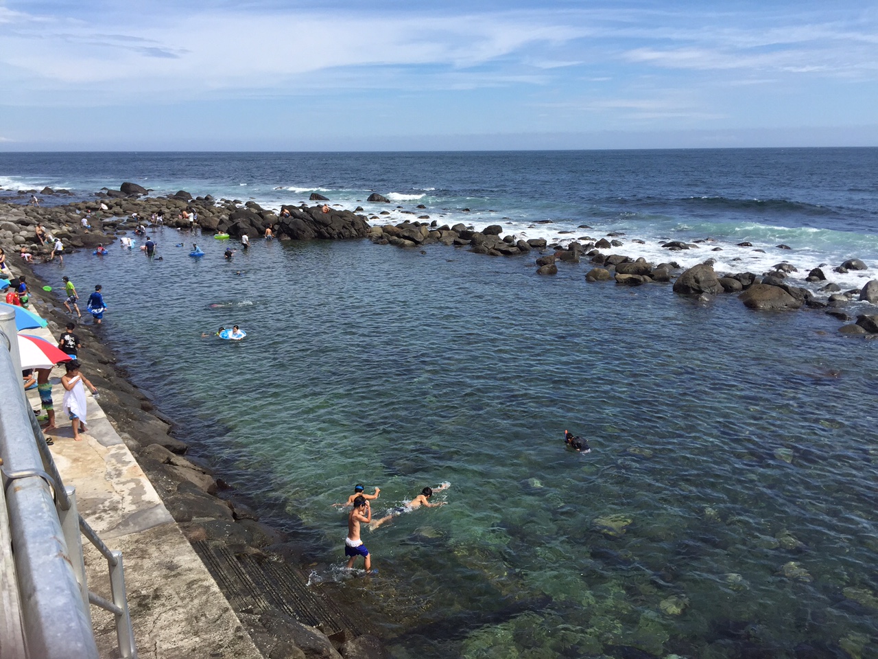 岩場に囲まれた海の自然プールで子供たちが海水浴を楽しんでいる写真
