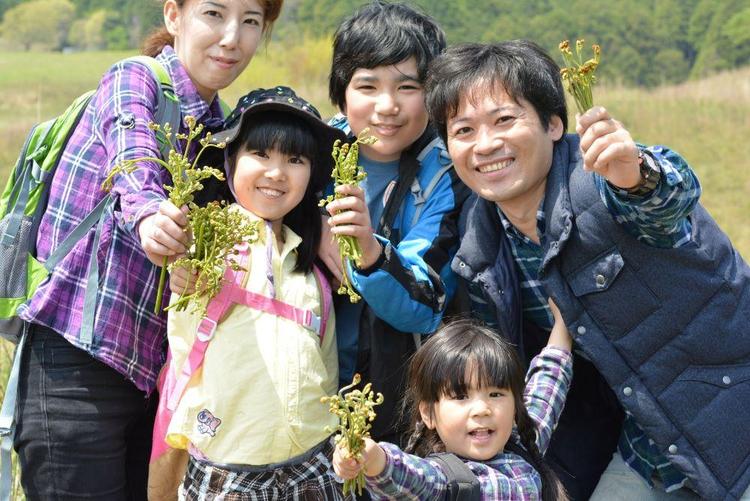 狩った山菜を手に持ちながら笑顔で写る5人家族の写真