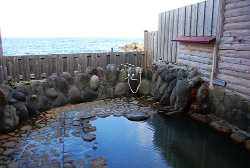 木と岩に囲まれた海の見える開放的な露天風呂の写真