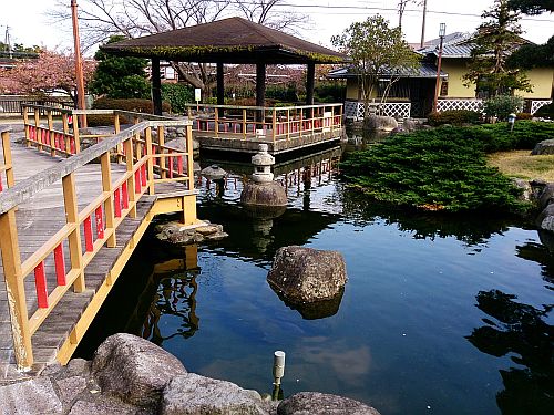 橋を渡った先にある、池の上に浮かぶ屋根付きの東屋の写真